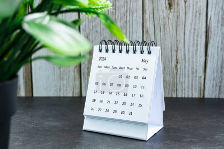 Weißer Kalender Mai 2024 auf Bürotisch aus Holz mit Topfpflanze. Neujahrskonzept 2024