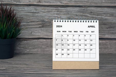Calendrier blanc avril 2024 sur bureau en bois avec plante en pot. Concept du Nouvel An 2024