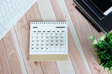 Weißer Januar 2024 Kalender auf Holztisch mit Tastatur, Notizbüchern, Bleistift, Topfpflanze und Smartphone.