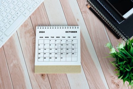 Foto de Blanco Octubre 2024 calendario en escritorio de madera con teclado, cuadernos, lápiz, maceta de la planta y el teléfono inteligente. - Imagen libre de derechos