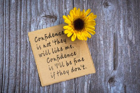 Photo for Motivational on brown note with gerbera yellow flower on wooden surface - Confidence is not they will like me, confidence is i will be fine if they do not. - Royalty Free Image