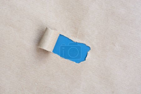 Braunes Papier mit gerissenem Loch und gerolltem Rand mit blauem Hintergrund.