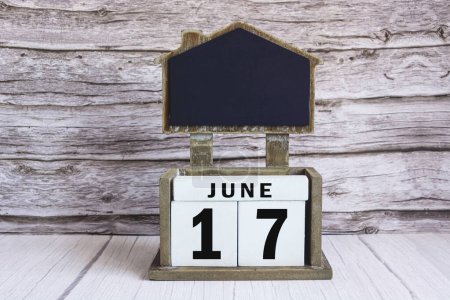 Chalkboard with June 17 calendar date on white cube block on wooden table.