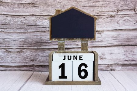 Chalkboard with June 16 calendar date on white cube block on wooden table.