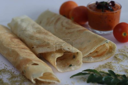 Téléchargez les photos : Thin crispy Indian crepe made of brown top millet and lentils. A healthy gluten free fermented breakfast dish with millet, called millet ghee roast dosa. Served with spicy tomato condiment. - en image libre de droit