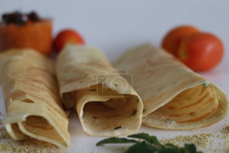 Photo for Thin crispy Indian crepe made of brown top millet and lentils. A healthy gluten free fermented breakfast dish with millet, called millet ghee roast dosa. Served with spicy tomato condiment. - Royalty Free Image