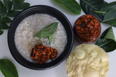 Photo for Kanji and Kadumanga. Rice gruel prepared with Matta rice. Served in earthen pot in a traditional way with spoon made of jackpot tree leaf. Shot with raw banana curry, cut mango pickle and pappad. - Royalty Free Image