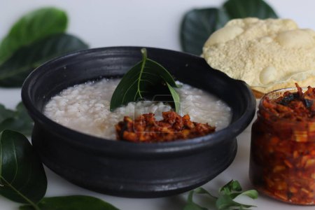 Photo for Kanji and Kadumanga. Rice gruel prepared with Matta rice. Served in earthen pot in a traditional way with spoon made of jackpot tree leaf. Shot with raw banana curry, cut mango pickle and pappad. - Royalty Free Image