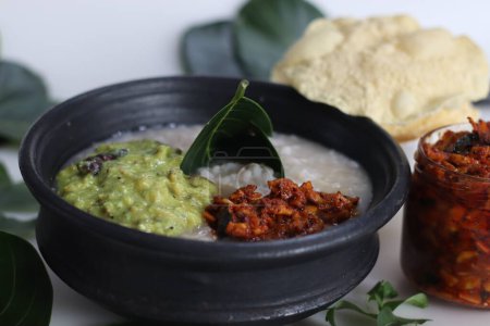 Téléchargez les photos : Kanji et Kadumanga. Gruau de riz préparé avec du riz Kerala Matta. Servi dans un pot en terre avec couverts en feuilles d'arbre jackpot. Tourné avec cornichon de mangue coupé, curry plantain cru avec noix de coco et épices et pappad - en image libre de droit
