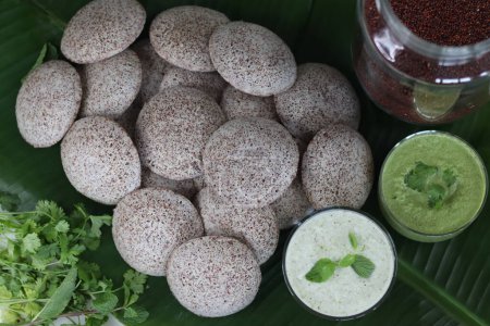 Photo for Ragi idly. Steamed savory rice cake made by a batter of fermented de husked black lentils and finger millets served with green chilly coconut condiments. Shot on green plantain leaf as background - Royalty Free Image