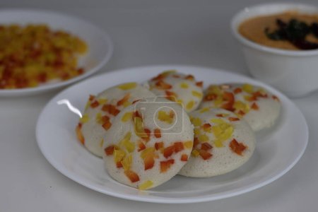 Foto de Pimiento salado servido ociosamente con chutney de coco. Un colorido y apetitoso desayuno del sur de la India. Pastel de arroz salado al vapor hecho con masa fermentada de lentejas y arroz cubierto con pimientos - Imagen libre de derechos
