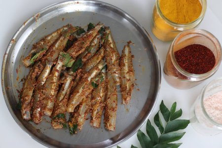Photo for Freshly cut, cleaned and marinated anchovy fish presented on a steel plate along with chili powder, pepper, ginger garlic paste and salt for marination, surrounded with fresh curry leaves. - Royalty Free Image