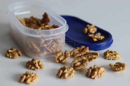 Pristine pile of premium dry walnuts in a plastic container, ideal for culinary creations and healthy snacks. Nut lovers rejoice in this bountiful harvest. Rustic, organic. Shot on white background