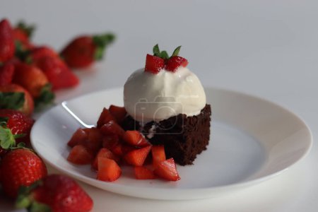 Chocolate brownie with fresh strawberries and a scoop of creamy vanilla ice cream, perfect for dessert menus and sweet cravings. Featuring Egg less preparation of brownie. Shot on white background