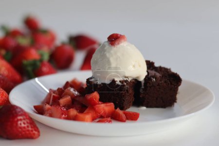 Chocolate brownie with fresh strawberries and a scoop of creamy vanilla ice cream, perfect for dessert menus and sweet cravings. Featuring Egg less preparation of brownie. Shot on white background