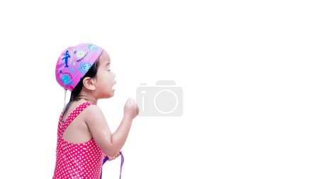 Photo for Girl Plays in the Water,Child Closes her Eyes and Water gets into her Eyes,Children Holds Purple Swimming Goggles,Kid Wears Red Swimsuit and Pink Swimming Cap. Baby aged 3 years. Isolated background. - Royalty Free Image