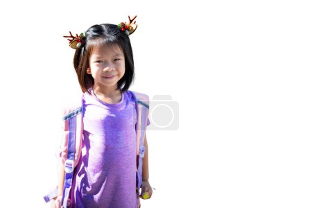 Foto de Chica joven con cuernos de reno y llevar una mochila, Niño alegre asiático con ropa morada y cornamenta de reno alfiler de pelo, aislado sobre un fondo blanco. - Imagen libre de derechos