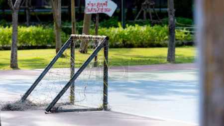 Ein kleines Futsal-Tor steht auf einem Übungsplatz in einem öffentlichen Park, ein verschwommenes Schild in roten thailändischen Buchstaben auf weißem Grund lautet: "Rauchen im Park verboten.."