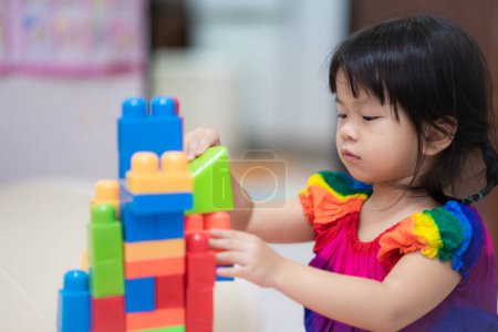 Nettes asiatisches Mädchen hat Spaß dabei, mit bunten Plastikklötzen zu spielen, eine Aktivität, die das Lernen fördert und Spaß und pädagogische Aktivität, Handmuskeln und Fantasie fördert. Kind im Alter von 3-4 Jahren.