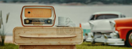 Photo for Radio, retro style, on wooden table, minimal, with coffee cup, background, vintage car and river.3 dimensions and illustrations - Royalty Free Image