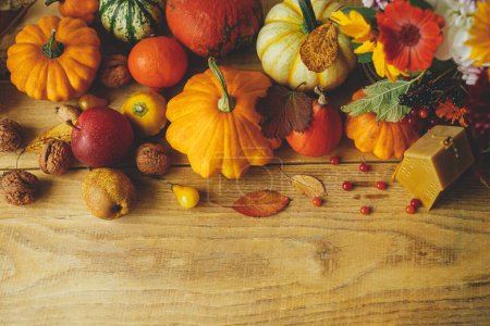 Happy Thanksgiving! Stylish pumpkins, autumn flowers, berries, leaves, candle on wooden table, rustic flat lay. Atmospheric autumn still life. Seasons greeting card template with space for text