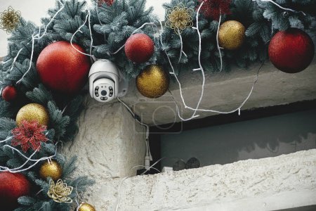 Photo for Stylish safety camera and christmas baubles on fir branches on building exterior. Modern christmas decor and security equipment in city street. Winter holidays in Europe. - Royalty Free Image
