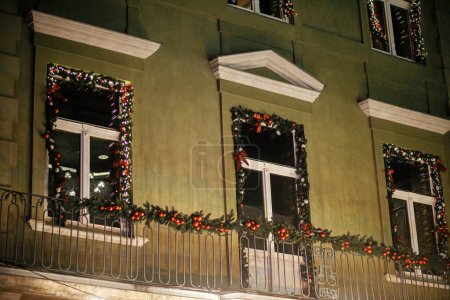Téléchargez les photos : Branches élégantes de sapin de Noël avec des boules et des lumières festives sur le bâtiment extérieur en soirée. Décor de Noël moderne dans la rue de la ville. Vacances d'hiver atmosphériques en Europe. Joyeux Noël - en image libre de droit