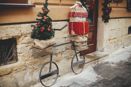 Vélo minimaliste élégant avec arbre de Noël et cadeaux enveloppés dans des paniers à l'extérieur du bâtiment. Décor de Noël moderne dans la rue de la ville. Vacances d'hiver en Europe. Joyeux Noël