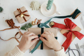Hands wrapping stylish christmas gift flat lay. Person preparing  christmas present with green ribbon and ornaments composition on white wood. Merry Christmas! Aesthetic winter holidays Poster #621046444