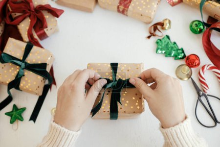 Foto de Persona preparando una moderna caja de regalo con cinta verde, papel de regalo dorado, adornos sobre fondo blanco. ¡Feliz Navidad! Manos envolviendo elegante regalo de Navidad plana laico. Tiempo de invierno atmosférico - Imagen libre de derechos