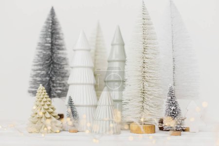 Foto de Feliz Navidad y Felices Fiestas! Pequeños árboles de Navidad con estilo sobre fondo blanco. Escena navideña festiva, bosque nevado en miniatura. Decoraciones de escándalos mínimos modernos, banner de vacaciones - Imagen libre de derechos