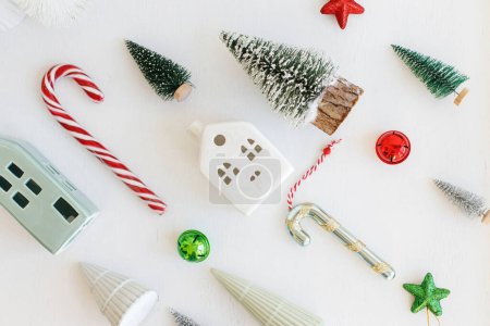 Photo for Christmas flat lay composition with stylish little christmas trees, houses, candy cane on white table. Merry Christmas and Happy Holidays! Modern festive winter banner, scandi decorations - Royalty Free Image