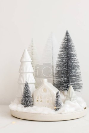 Photo for Modern christmas scene, miniature snowy village on white table. Merry Christmas! Stylish little Christmas trees and house. Winter hygge, scandinavian  monochromatic decor. - Royalty Free Image