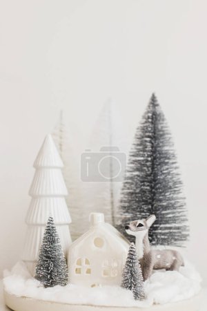Téléchargez les photos : Joyeux Noël ! Petits arbres de Noël élégants et jouet de renne sur table blanche. Scène de fée de Noël, forêt enneigée miniature avec des cerfs mignons. Cadre de table moderne, décorations monochromes - en image libre de droit