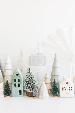 Téléchargez les photos : Joyeux Noël ! Petits arbres de Noël élégants et maisons décorations sur table blanche. Scène de Noël moderne, village enneigé confortable miniature. Bannière vacances d'hiver, décor scandinave - en image libre de droit