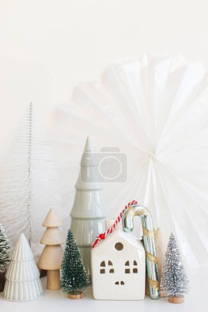 Photo for Stylish little Christmas trees, houses and candy cane on white table. Merry Christmas and Happy Holidays! Modern festive scene, miniature snowy village. Winter banner, scandinavian decor - Royalty Free Image