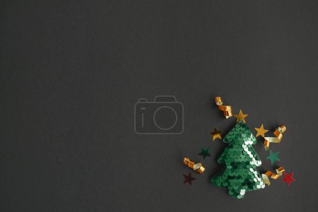 Téléchargez les photos : Arbre de Noël moderne minimum plat laïc, concept de vacances d'hiver. Élégant petit arbre de Noël avec des confettis d'or scintillant sur fond noir. Joyeux Noël ! Espace pour le texte. Idée créative - en image libre de droit