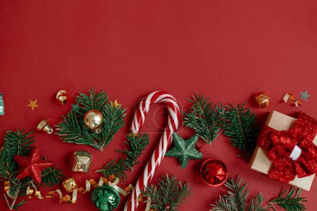 Téléchargez les photos : Joyeux Noël ! Pose appartement moderne de Noël. Cadeau de Noël élégant, boules, branches de sapin, confettis et canne à bonbons sur fond rouge. Modèle de carte de voeux Saisons, espace pour le texte. Vacances d'hiver - en image libre de droit