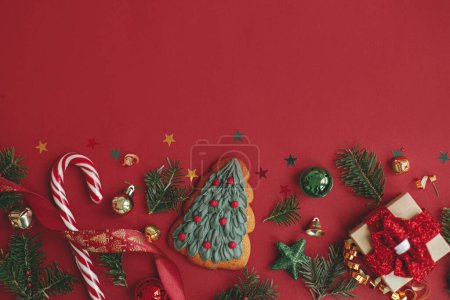 Téléchargez les photos : Appartement de Noël moderne laïc. Élégant biscuit d'arbre de Noël, cadeau, boules, branches de sapin, confettis sur fond rouge. Carte de vœux des saisons, espace pour le texte. Joyeux Noël ! Vacances d'hiver - en image libre de droit