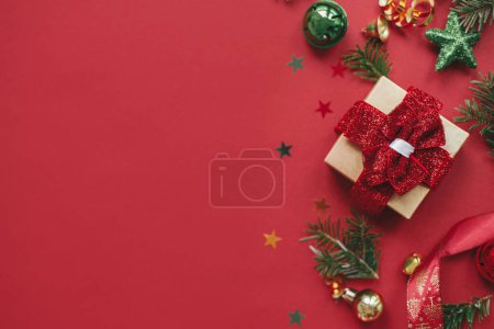 Téléchargez les photos : Joyeux Noël ! Appartement de Noël moderne laïc. Cadeau de Noël élégant, boules, branches de sapin, confettis sur fond rouge. Carte de vœux des saisons, espace pour le texte. Bannière vacances d'hiver - en image libre de droit