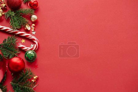 Foto de ¡Feliz Navidad! Moderno piso de Navidad. Elegante bastón de caramelo de Navidad, adornos, ramas de abeto, confeti sobre fondo rojo. Tarjeta de felicitación Seasons, espacio para texto. Banner de vacaciones de invierno - Imagen libre de derechos