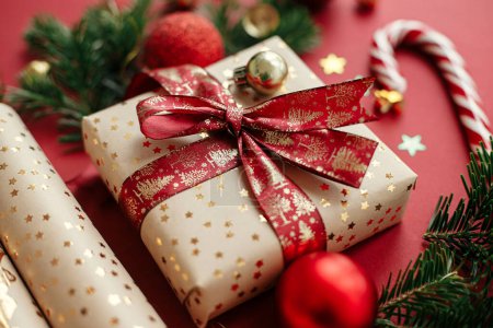 Téléchargez les photos : Joyeux Noël et Joyeuses Fêtes ! Composition moderne de Noël. Cadeau de Noël élégant, papier d'emballage, branches de sapin, canne à bonbons et boules sur fond rouge. Bannière festive - en image libre de droit