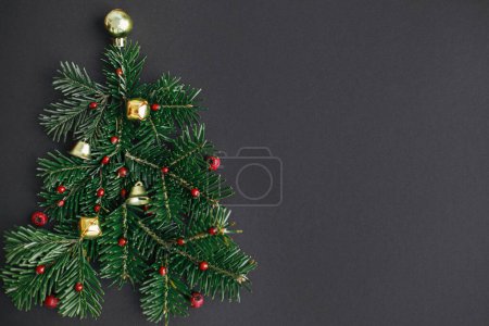 Téléchargez les photos : Arbre de Noël, concept vacances d'hiver. Élégant arbre de Noël composé de branches de sapin, de baies rouges et de boules d'or sur fond noir, plat. Idée créative. Bannière festive moderne - en image libre de droit