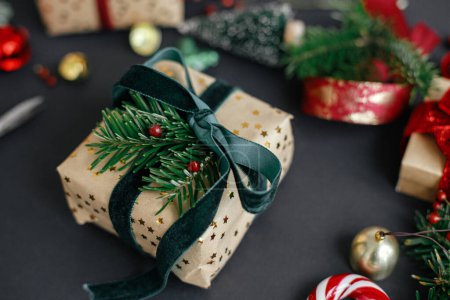 Téléchargez les photos : Joyeux Noël et Joyeuses Fêtes. Élégant cadeau de Noël avec ruban vert et branche de sapin sur fond noir avec des décorations festives modernes. Cadeau de Noël moderne - en image libre de droit