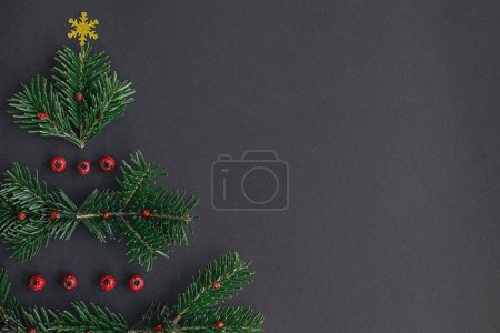 Foto de ¡Feliz Navidad! Elegante árbol de navidad hecho de ramas de abeto, bayas rojas y estrella dorada sobre fondo negro, tendido plano con espacio para el texto. Idea creativa del árbol de Navidad. Banner de vacaciones de invierno - Imagen libre de derechos