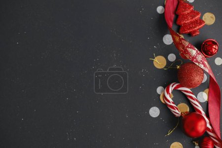 Téléchargez les photos : Appartement de Noël moderne laïc. Élégantes canne à bonbons de Noël, confettis et boules rouges bordent sur fond noir. Carte de vœux de saison, espace pour le texte. Joyeux Noël ! Bannière vacances d'hiver - en image libre de droit