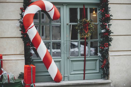 Photo for Stylish big candy cane, red and green wrapped christmas gifts, fir branches, wreaths on building exterior. Modern christmas decor in city street. Winter holidays in Europe. Merry Christmas - Royalty Free Image