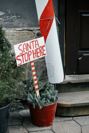 Photo for Stylish big candy cane and sign Santa stop here at building exterior. Modern christmas decor in city street. Winter holidays in Europe. Festive decorations - Royalty Free Image
