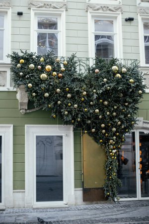 Photo for Stylish christmas fir branches with green and gold baubles and lights on building exterior. Modern christmas decor in city street. Winter holidays in Europe. Merry Christmas - Royalty Free Image