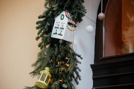Téléchargez les photos : Branches élégantes de sapin de Noël avec lanterne, boules et lumières sur l'extérieur du bâtiment. Décor de Noël simple moderne dans la rue de la ville. Vacances d'hiver en Europe. Joyeux Noël - en image libre de droit